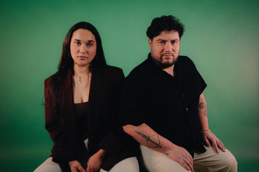 Ema en Andrés zittend naast elkaar, recht in de lens, groene achtergrond